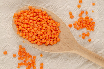 Red lentils with a wooden spoon on a linen napkin, close-up, top view.