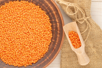 Red lentils in a ceramic plate with a wooden spoon on a wooden table, close-up, top view.