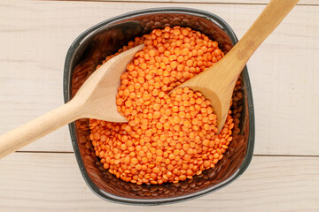 Red lentils in a ceramic plate with a wooden spoon on a wooden table, close-up, top view.