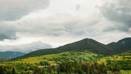 Fototapeta premium Dramatic clouds gather over the rolling green hills of the Carpathian Mountains on an overcast day.