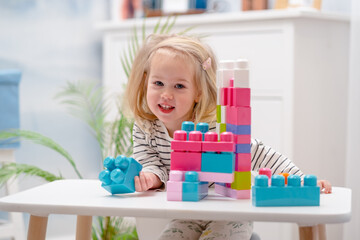 A little child girl plays a sorter, a construction kit, or an educational game at a table in a room