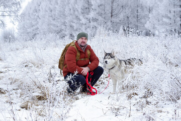 A blue-eyed husky and his owner in an amazing winter shoot. A mature Caucasian man, holding a pet on a leash, poses in front of the camera. © Dmitrii Labrador