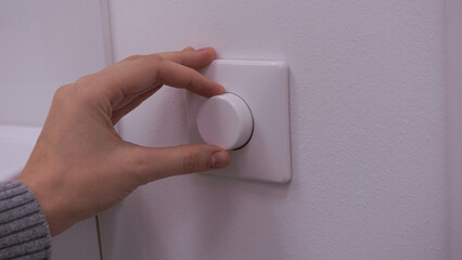 Hand adjusting brightness or turning down electrical light dimmer switch. Saving energy concept. Close up
