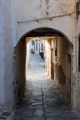 Narrow alley with tunnel and with whitewashed walls and stone pavement leading to a courtyard in...