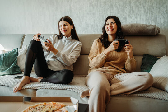 Young caucasian woman and her sister play video games on joystick and eat pizza