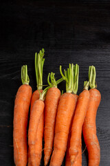 Aerial view of carrots with stem on dark wooden table, vertical with copy space