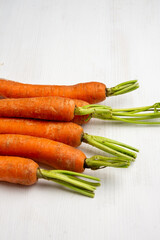 Top view of carrots with stem on white wooden table, vertical with copy space