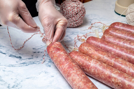 A cook wearing rubber gloves ties a sausage with a rope.