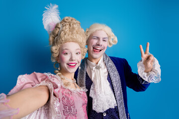 A joyful couple in historical attire posing against a vibrant blue background, expressing happiness and camaraderie
