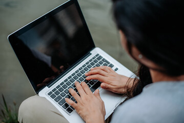 A woman sitting by a lake, typing on a laptop in a calm, natural setting, balancing remote work...