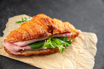 Croissant sandwich ham, cheese, green leaf salad delicious gourmet food background on the table rustic food top view copy space