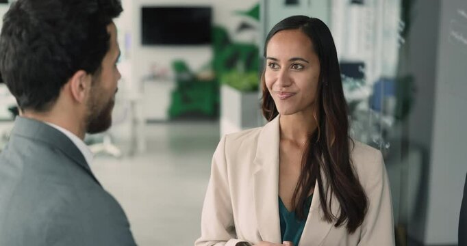 Positive young business professional woman talking to male colleague on work break, standing in office space, speaking to man, smiling, discussing job, career, enjoying corporate communication