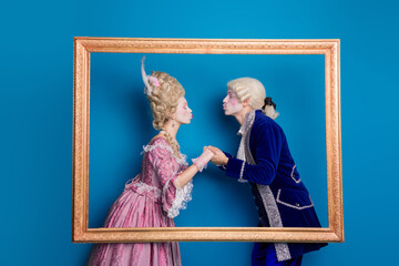 Elegant couple in vintage attire posing within a golden frame against blue background, portraying a...