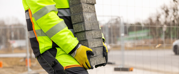 Construction worker carrying paving stones at road construction site
