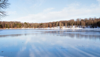 Obraz premium Frozen pond reflecting clear sky and bare trees, serene winter landscape