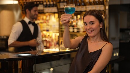 Sitting beautiful woman guest looking at camera to pose with drinking mixed vodka in blue hawaii...