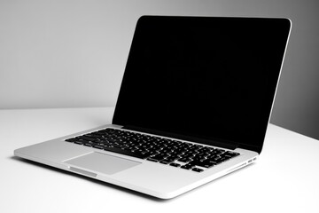Fototapeta premium A sleek silver laptop with a black screen sits on a white table against a neutral background.