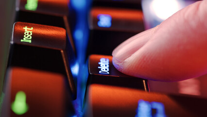 Human finger clicks on the Delete key on the computer keyboard, close up view. Man finger presses Delete on the keyboard key, macro shot. Rgb led light keyboard