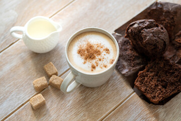 Cappuccino coffee with cinnamon and chocolate chip muffin on a wooden table, coffee break