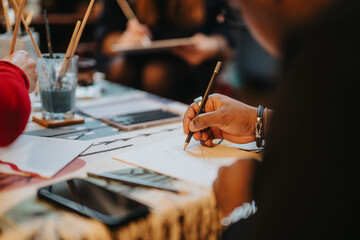 The image captures a close-up of a hand sketching, emphasizing creative expression in a workshop environment. Art supplies and a vibrant atmosphere surround the scene, inspiring creativity.