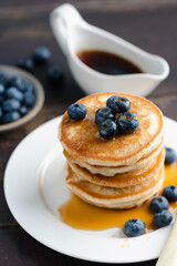 Pancakes with blueberries stack on white ceramic plate served with maple syrup, closeup view