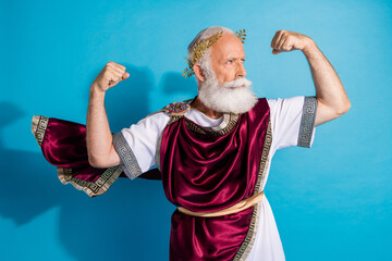 Photo of handsome senior male show strong muscles wear ancient greek god king dress isolated on blue color background