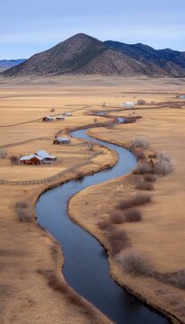 Aerial view of winding river through a rural valley with weathered farmhouses and mountains in the background