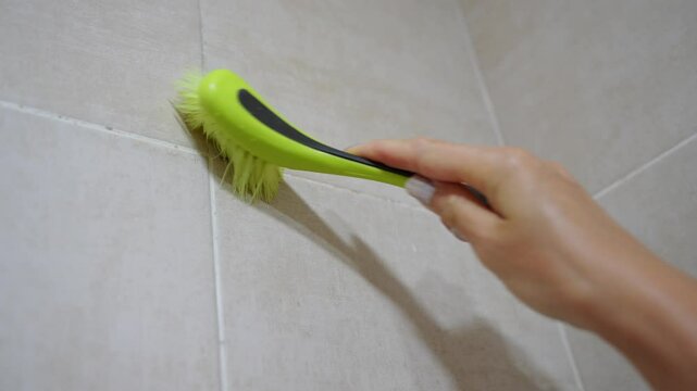 Cleaning black mold on grout between bathroom tiles with squeegee in damp, poorly ventilated bathroom, close-up. Dampness problem in bathrooms, getting rid of mold indoors