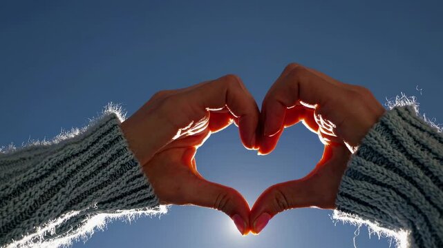 Low-angle video shot of hands forming a heart shape against a clear blue sky, emphasizing warmth and connection with a cozy, intimate style.