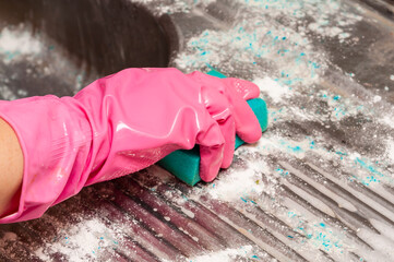 Pink gloved hand cleans a dirty surface with a sponge, soap and remnants of cleaning agent.