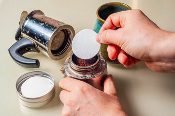 Hands prepare a Moka pot with a paper filter to brew fresh coffee at home for a mug.