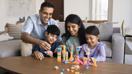 Indian couple playing construction blocks set together with little children. Siblings sit on floor...