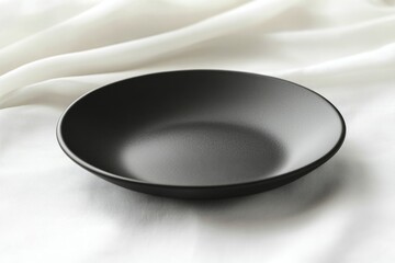 A sleek, empty, black plate rests on a white fabric background, creating a minimalist aesthetic.