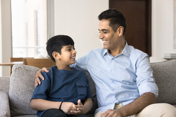 Mature dad lead pleasant conversation with school-age son seated on sofa in living room, spend...