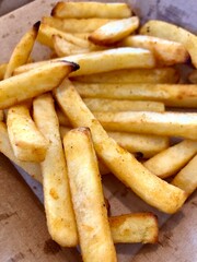 Close up of a pile of french fries. Fried potatoes on a cardboard plate. Junk food illustration.