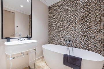 Stylish bathroom interior design. The bathtub is against a wall decorated with dark mosaic .tiles.