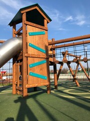 Empty new wooden playground on a sunny morning. No one on the swings, slide or net.