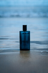 A stylish blue perfume bottle stands in shallow ocean water with gentle waves surrounding it. The...