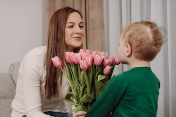A loving boy hugs his mother and gives her pink tulips. A happy, tender moment perfect for Mother's...