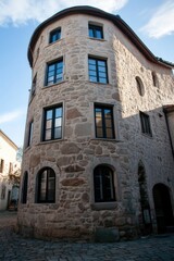 Fototapeta premium A distinctive round stone building stands majestically in a charming village, with the bright blue sky and fluffy clouds beautifully reflected in its windows