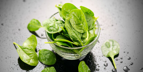 Spinach in a transparent glass bowl on gray background with reflection. Heap of Baby spinach fresh...