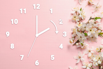 Clock and flowers on pink wooden background, top view. Arrow showing time change one hour ahead in...