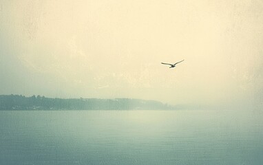 Fototapeta premium A small airplane flies over a calm body of water on a hazy day. The colors are muted greens, blues and beige. The scene is tranquil and serene