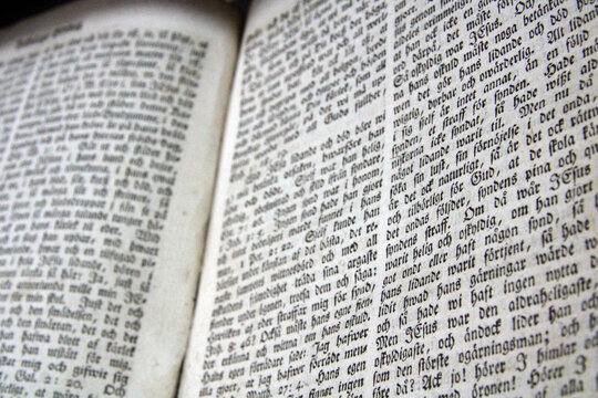 Close-up of an open antique book with dense blackletter text, showing aged pages and historical typography. Swedish language.