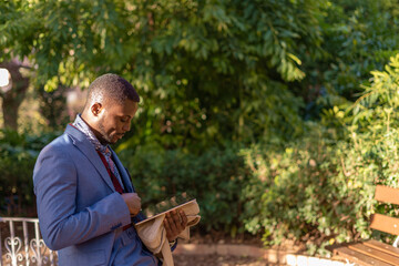 An elegant man is seen deeply engrossed in reading a book within a beautiful natural setting