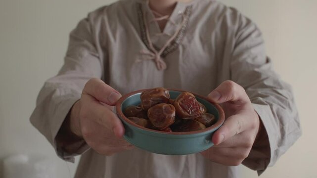 Young man dressed in traditional Middle Eastern clothing offering dates during Ramadan in slow motion