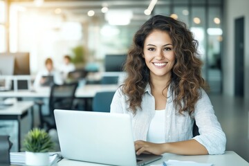 A smiling woman working on her laptop in a modern office space. She exudes confidence and positivity, contributing to a vibrant workplace atmosphere.