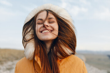 Happy woman in stylish orange coat with fur hood smiling outdoors in fashion and beauty shot