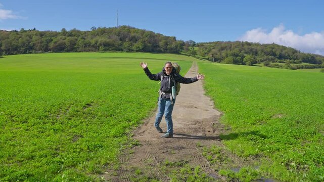 Happy and excited trekker looking at picturesque dirt path going through a lush green grass field with blue skies
