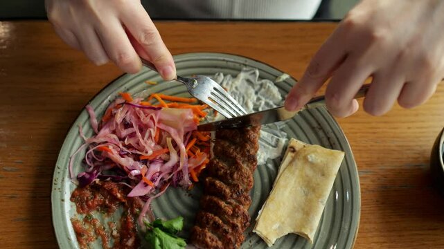 Woman cutting a piece of lula kebab with a knife and fork
